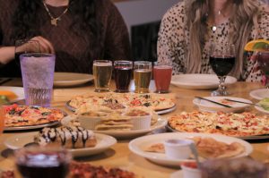 two women at table with feast of pizza, beer, wine, and sides on table